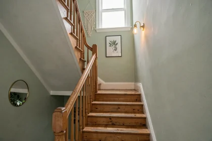 Cage d'escalier étroite avec mur peint en vert sauge, miroir rond et décoration murale botanique pour apporter de la clarté