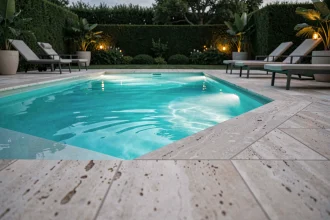 Piscine extérieure moderne avec éclairage subaquatique LED turquoise au crépuscule, reflets colorés sur les dalles en travertin
