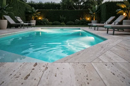 Piscine extérieure moderne avec éclairage subaquatique LED turquoise au crépuscule, reflets colorés sur les dalles en travertin
