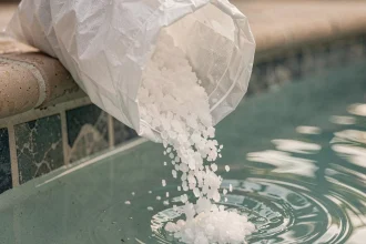 Cristaux de sel de piscine versés dans le skimmer d'une piscine résidentielle avec eau bleue en arrière-plan